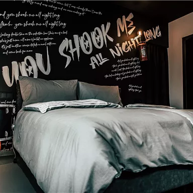 A modern bedroom with a large bed and a creative wall design. The wall is adorned with inspiring texts and graphics.