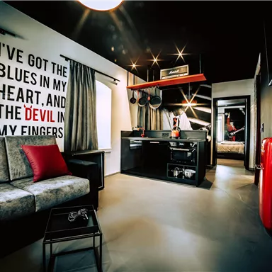 A modern room with a cozy sofa and a small kitchenette. On the wall, there is a striking text that conveys a musical atmosphere.