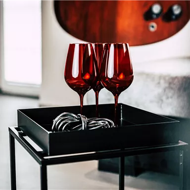 Three red wine glasses are standing on a black tray. Next to it is a cable that is neatly rolled up.