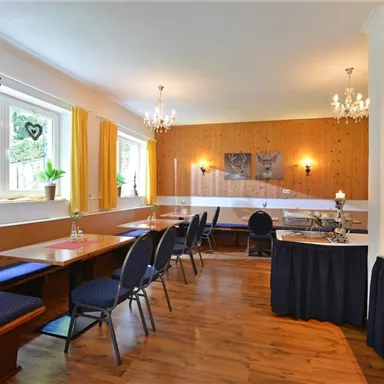Ein gemütlicher Essbereich mit Holztischen und blauen Stühlen. Die Wände sind geschmackvoll dekoriert und große Fenster lassen viel Licht herein.