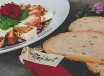 Ein leckerer Salat mit Tomaten, Mozzarella und frischen Basilikumblättern auf einem weißen Teller. Daneben liegen zwei Scheiben Brot auf einem Holzbrett.