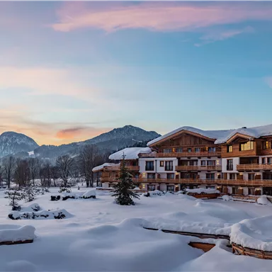 Eine gemütliche Berglandschaft mit einem verschneiten Hotel und einem malerischen Sonnenuntergang. Die Umgebung ist ruhig und von winterlichen Bäumen umgeben.