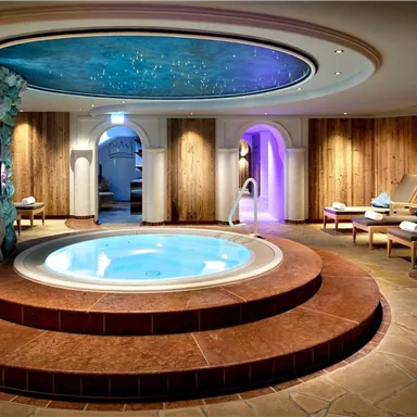 Ein eleganter Spa-Bereich mit einem runden Whirlpool und einem glitzernden Sternenhimmel. Entspannende Liegen und warme Holzverkleidungen schaffen eine ruhige Atmosphäre.