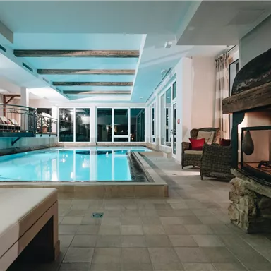 An elegant indoor pool with illuminated water and a cozy fireplace. The atmosphere is relaxing and inviting.