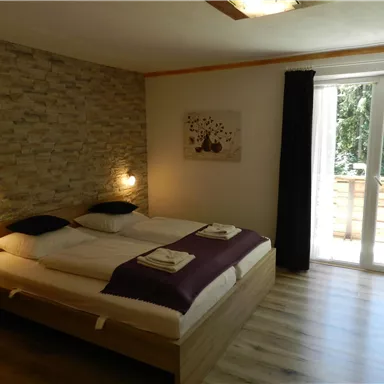 Ein gemütliches Schlafzimmer mit zwei Betten und modernen Möbeln. Große Fenster sorgen für viel Tageslicht und Blick auf einen Balkon.
