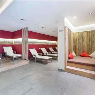A modern relaxation room with comfortable loungers and wooden details. The walls are painted in warm shades of red, creating an inviting atmosphere.