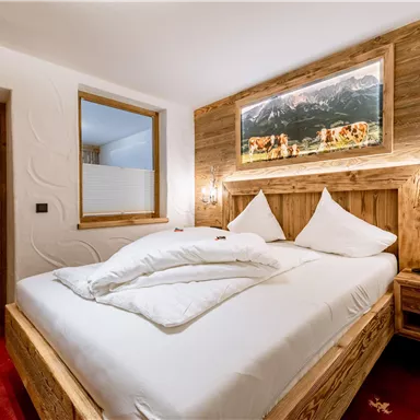 A cozy bedroom with a wooden bed and white pillows. The decorative wall and the picture give the room a warm atmosphere.
