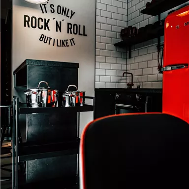 A modern kitchen with a red refrigerator and a stylish shelf.
On the wall is the saying "It's only rock 'n' roll, but I like it."