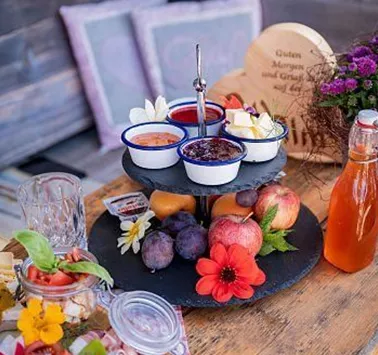Ein liebevoll angerichteter Dessertteller mit verschiedenen Saucen, frischen Früchten und blühenden Dekorationen. Daneben eine Flasche Saft und eine hübsch gestaltete Holzfigur.