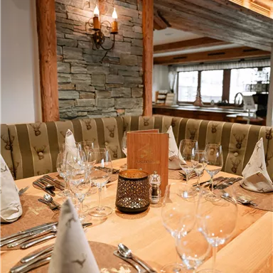 Ein eleganter Tisch in einem gemütlichen Restaurant mit Gläsern, Besteck und dekorativen Servietten. Die Wände sind aus Stein und Holz, was eine warme Atmosphäre schafft.