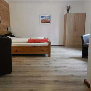Ein gemütliches Zimmer mit einem Holzbett und einem Sofa. Die Wände sind teilweise mit Holz verkleidet und es gibt einen Schrank sowie ein Bild an der Wand.