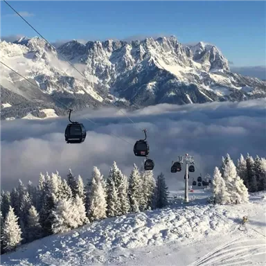 Eine eindrucksvolle Berglandschaft mit schneebedeckten Bäumen und Seilbahnen, die durch die Wolken fahren. Im Hintergrund sind majestätische Berge sichtbar.
