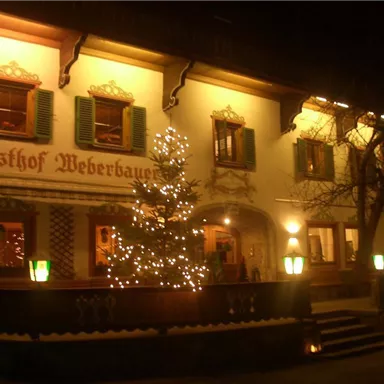 Ein traditionelles Gasthaus mit einem festlich geschmückten Weihnachtsbaum. Die Fassade ist beleuchtet und lädt die Gäste ein.