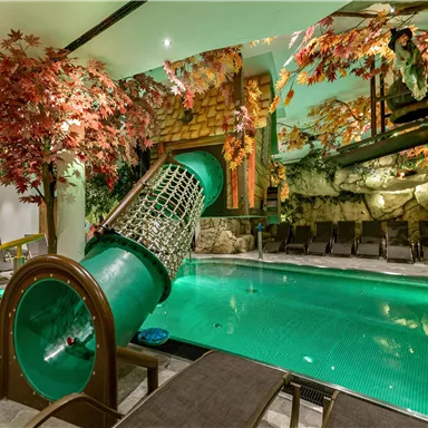 A swimming pool with a modern slide element and a decorative environment of colorful trees. The relaxing atmosphere is accentuated by the lighting and the natural design.