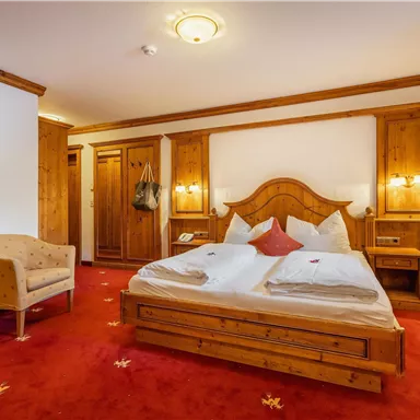 Ein gemütliches Schlafzimmer mit Holzmöbeln und einem Doppelbett. Der Boden ist mit rotem Teppich ausgelegt und es gibt einen bequemen Sessel.