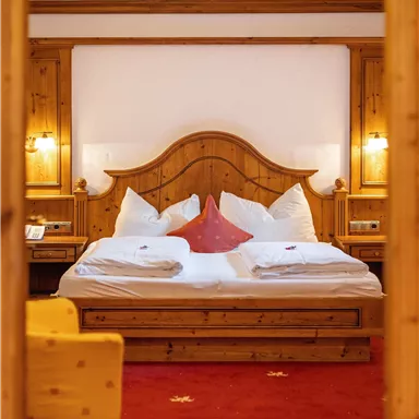 Ein gemütliches Schlafzimmer mit einem holzverzierten Bett und weißen Kissen. Der Boden ist rot mit einem Sternmuster und ein gelbes Sofa steht im Vordergrund.