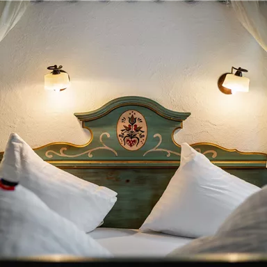 Ein gemütliches Schlafzimmer mit einem dekorativen Kopfteil und Kissen. Weiche Beleuchtung sorgt für eine entspannte Atmosphäre.