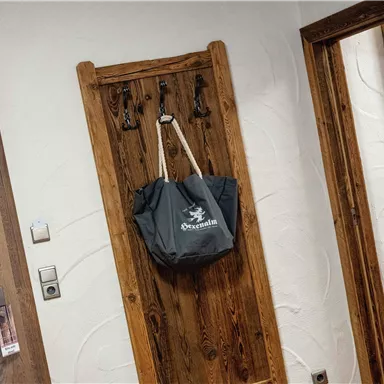 Ein Holzregal mit mehreren Haken, an dem eine graue Tasche hängt. Im Hintergrund sind zwei Türen und ein Spiegel sichtbar.