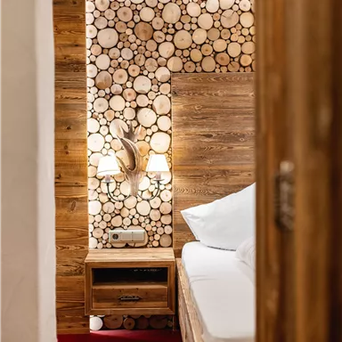 Ein gemütliches Schlafzimmer mit Holzdetails und einem rustikalen Wandarrangement aus Holzscheiten. Das rote Teppich sorgt für eine einladende Atmosphäre.