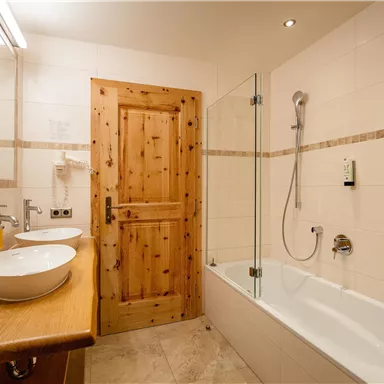 A modern bathroom with a wooden door and large mirrors. There is a bathtub, two sinks, and a shower.