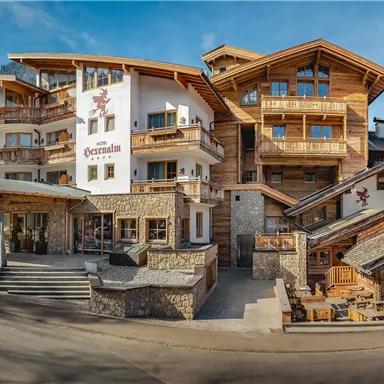 Ein charmantes Holzhaus mit mehreren Etagen in einer Berglandschaft. Die Umgebung ist ruhig mit einem klaren Himmel und Bergen im Hintergrund.
