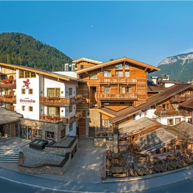 A picturesque mountain hotel with traditional wooden buildings, surrounded by green mountains. The sky is clear and the landscape radiates tranquility.