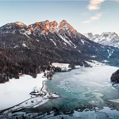 Eine bezaubernde Landschaft mit schneebedeckten Bergen und einem gefrorenen See. Der Himmel ist klar und die Farben des Sonnenuntergangs sind sichtbar.