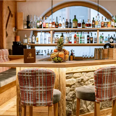 Eine gemütliche Bar mit Holzdetails und einer einladenden Sitzgelegenheit. Im Hintergrund sind Regale mit verschiedenen Getränken dekoriert.