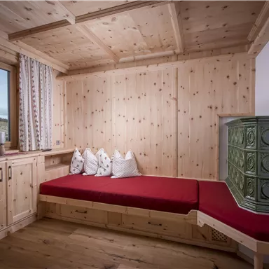 A cozy room with wood paneling and a red sofa. Through the window, there is a view of nature.