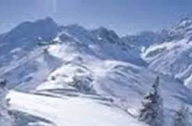 Eine schneebedeckte Berglandschaft unter einem klaren blauen Himmel. Die Sonne strahlt hell und verleiht der Szene einen funkelnden Glanz.