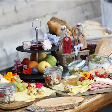 A rich breakfast buffet with various types of cheese, ham, fresh fruits, and jams. Bread and desserts are also beautifully arranged on a wooden tray.