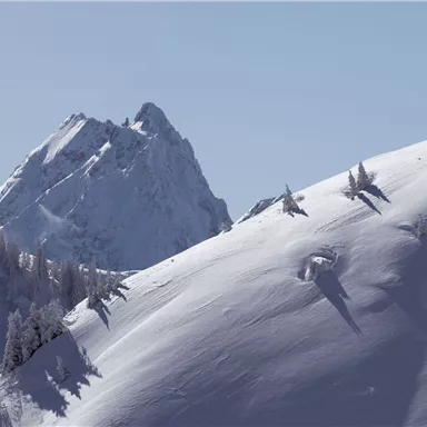Eine schneebedeckte Berglandschaft mit einem hohen Gipfel im Hintergrund. Der Himmel ist klar und blau, was eine ruhige Atmosphäre schafft.