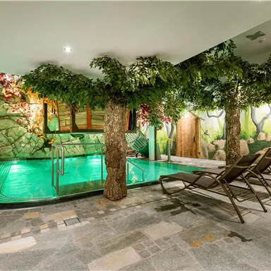 A luxurious indoor pool in a relaxing environment with artistic trees and nature motifs. Loungers are available for relaxation.