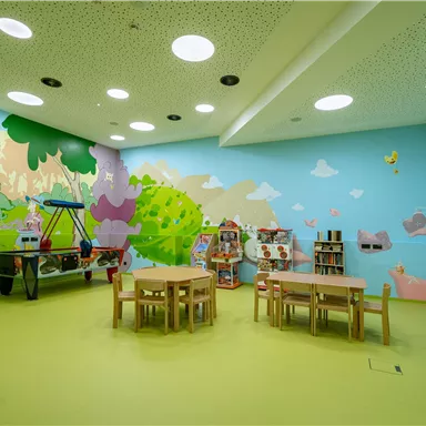 A colorful playroom with bright walls and cheerful motifs. There are tables and chairs as well as toy shelves.