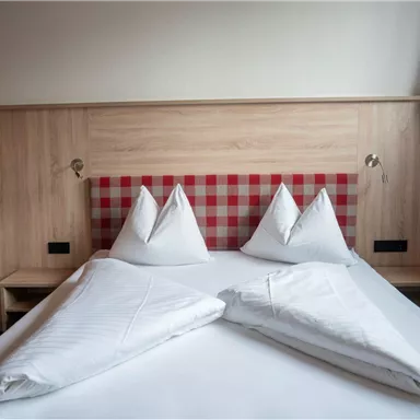 Ein gemütliches Schlafzimmer mit einem Doppelbett und einer Holzverkleidung. Die Kissen sind formschön gefaltet und die Wände haben eine helle, freundliche Farbgestaltung.