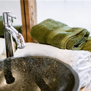 A modern stone sink with shiny faucets. On it lie clean, green, and white towels.