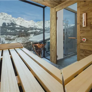 Eine moderne Sauna mit Holzliegen und Blick auf schneebedeckte Berge. Das große Fenster lässt viel Tageslicht herein und bietet eine entspannte Atmosphäre.