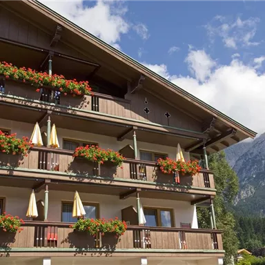 A charming wooden house with many balconies adorned with colorful flowers. In the background, a majestic mountain panorama can be seen.