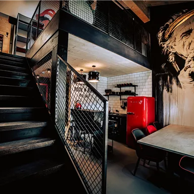 A modern, stylish interior with a wooden staircase and a red refrigerator in an open kitchen. An impressive mural can be seen on the wall.