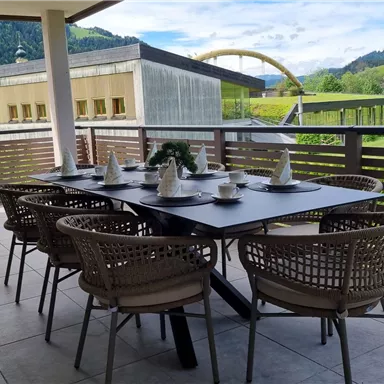 Ein geschmackvoll eingerichteter Esstisch auf einer Terrasse mit Blick auf grüne Hügel und Berge. Der Raum ist hell und einladend, ideal für gesellige Mahlzeiten im Freien.