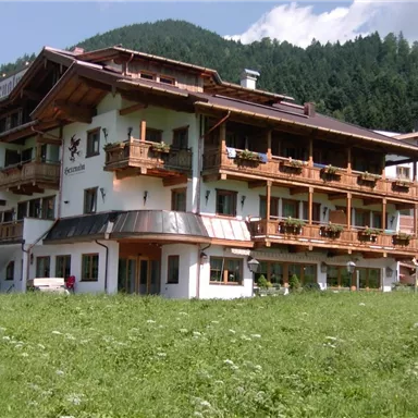 Ein charmantes Gebäude im alpinen Stil mit mehreren Balkonen. Umgeben von grünen Wiesen und Bergen im Hintergrund.
