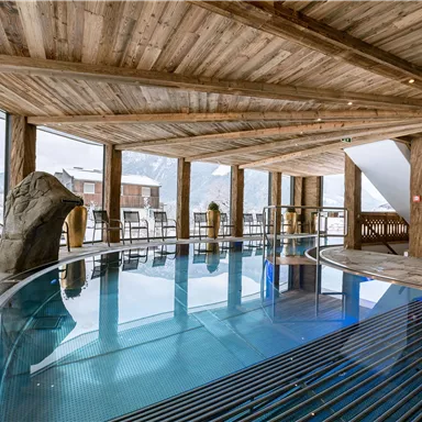 An elegant indoor pool in a rustic wooden building. Large windows offer a view of the snow-capped mountains.