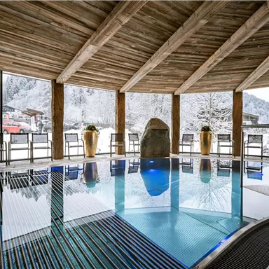 Ein Innenpool in einer Holzhütte mit großen Fenstern und Blick auf verschneite Berge. Entspannung und Ruhe in einer gemütlichen Atmosphäre.