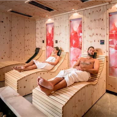 A beautiful relaxation room with wooden paneling and illuminated walls. Two people are lying on loungers and enjoying the tranquility.