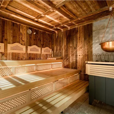 Eine gemütliche Sauna mit Holzverkleidung und Bänken. Am Wand hängt eine Kupferkelle über einem Heizofen.