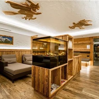 Ein gemütlicher Raum mit Holzmöbeln und einem zentralen Aquarium. Deckenverzierungen und eine warme Beleuchtung sorgen für eine einladende Atmosphäre.