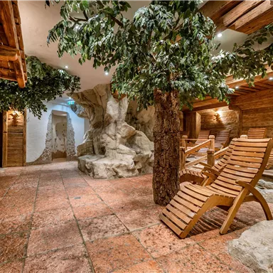 Ein entspannender Wellnessbereich mit Holzmöbeln und künstlichen Bäumen. Sanfte Beleuchtung schafft eine ruhige Atmosphäre.