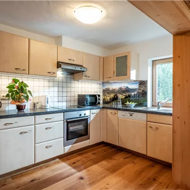 Eine moderne Küche mit Holzschränken und einem hellen Arbeitsbereich. Ein Fenster lässt natürliches Licht herein und es gibt eine Pflanze auf der Arbeitsfläche.