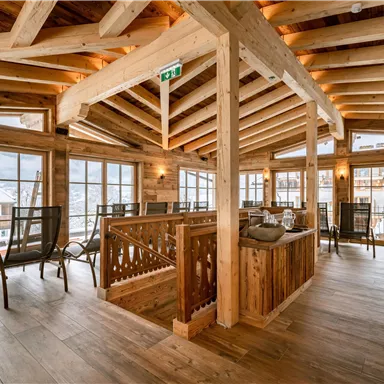 Ein modernes Holzinterieur mit großen Fenstern und gemütlichen Lounge-Stühlen. Der Raum bietet viel Tageslicht und eine einladende Atmosphäre.