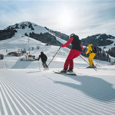 Drei Skifahrer genießen die Piste in einer winterlichen Landschaft. Die Sonne scheint über den schneebedeckten Bergen.